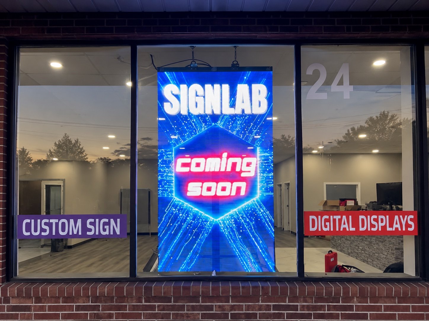 SignLab Troy storefront window with a transparent LED display showing coming soon content