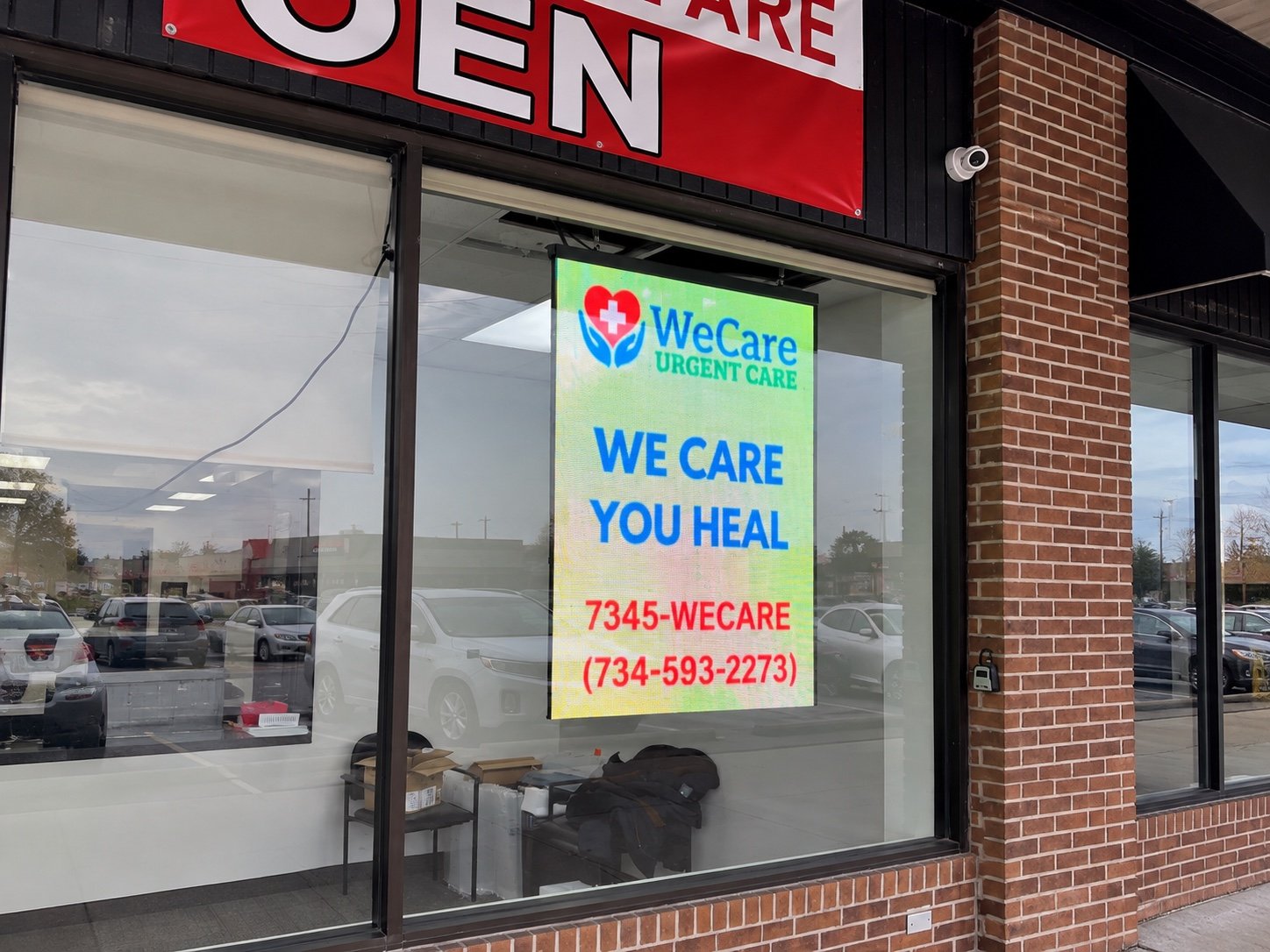 WeCare Urgent Care transparent LED window display showing clinic contact information